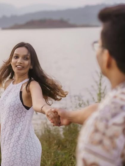 A classic 'follow me to' style shot, with the woman leading her partner towards the beautiful lakeside view.