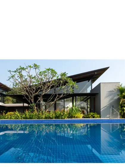A view across the pool at a home in Alibaug. The design uses sloped solar fin roofs and high ceilings to allow for thermal stack release and convectional cooling.
