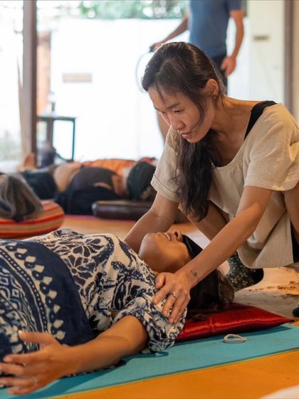A beautiful moment from a breathwork workshop, where facilitator Gon provides gentle, supportive touch to a participant in a state of deep relaxation.