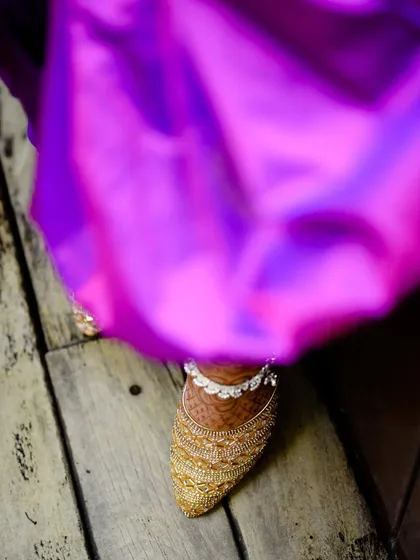 A detail shot of the bride's elegant footwear and the beautiful silver anklet, peeking out from under her rich purple saree.
