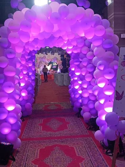 A stunning balloon tunnel entrance for a butterfly-themed party, lit with purple lights to create a magical entryway for guests.