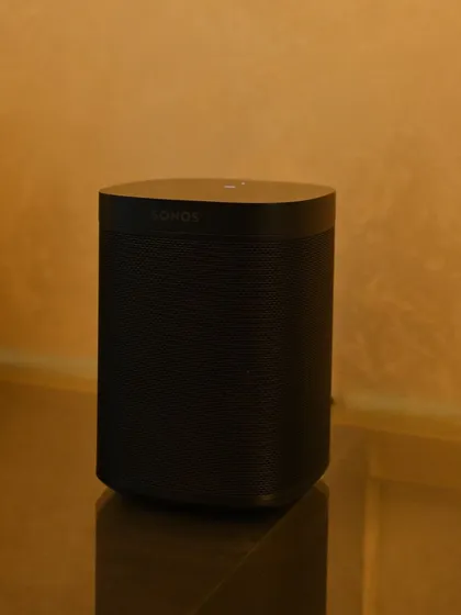 A modern Sonos speaker placed on a glass shelf. Its clean, minimal design allows it to fit into any contemporary home, providing high-quality wireless audio without disrupting the room's elegant and warm aesthetic.
