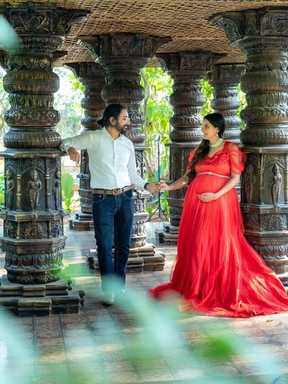 A lovely wide shot of a couple standing among carved pillars. The mom-to-be's red gown provides a beautiful contrast to the setting.