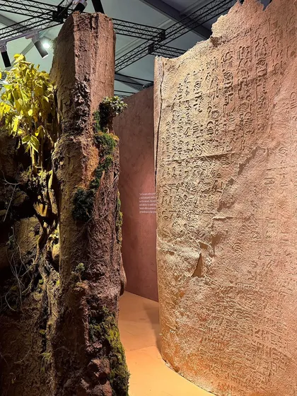 A detail shot of the 'Soil' installation, where a structure covered in moss and foliage stands next to a wall with ancient-looking script. This juxtaposition explores the relationship between nature and civilization.