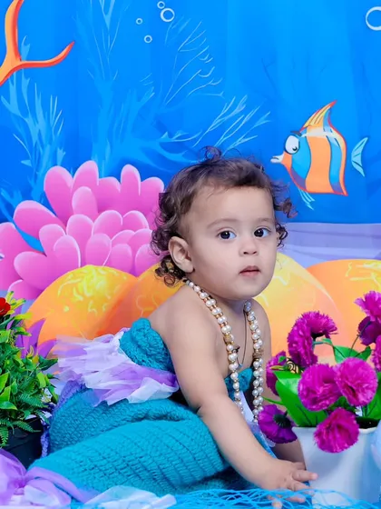A close-up of our little mermaid, looking curiously at the camera amidst a colorful underwater world.