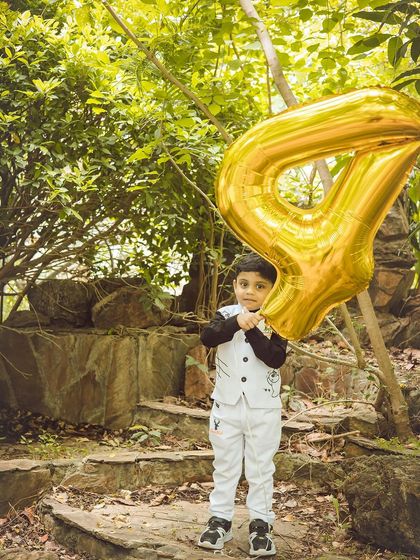 A sweet portrait of the birthday boy holding his golden '4' balloon. The natural light beautifully illuminates his happy face.