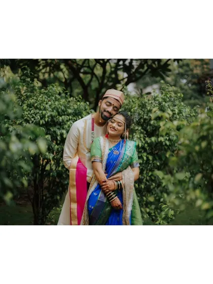 Framed by lush green leaves, this portrait has a beautiful, natural feel. The couple's embrace and the bride's vibrant blue and green Paithani saree stand out against the verdant background.