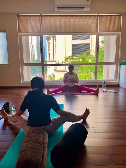 A student receives guidance in a wide-legged seated forward fold. This one-on-one attention helps deepen the stretch and prevent injury.