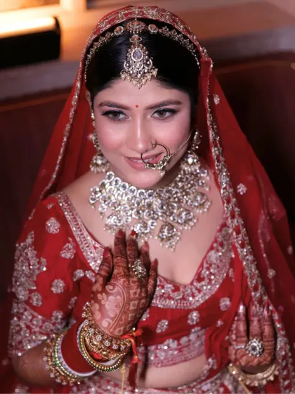 This bride's look is a blend of tradition and personal style. The makeup features a radiant base and defined eyes, perfectly complementing her red lehenga and unique peacock feather accessory.