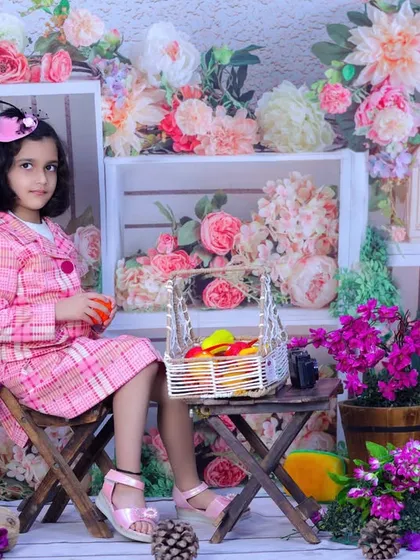 A full view of our floral garden theme, with a girl sitting at a small table holding a basket of fruit. A vibrant and fresh setting for a child's portrait.