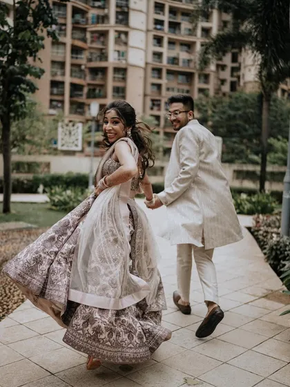 A fun, candid "follow me" shot taken during an engagement session in a modern residential area. The bride's joyful glance back and the movement in her lehenga capture the excitement of the moment.