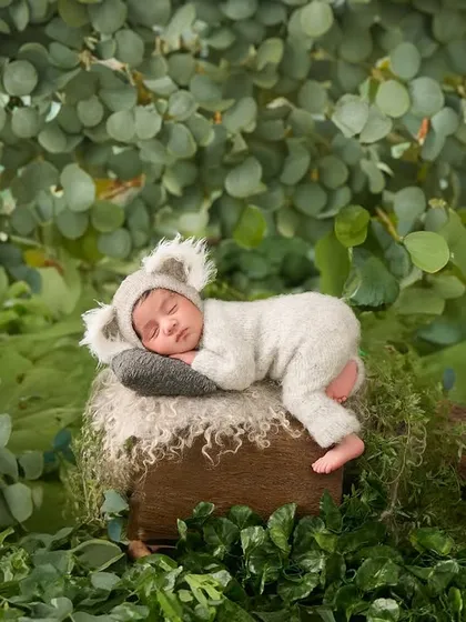 Showcasing our playful side, this adorable baby is dressed in a koala outfit, napping in a lush, leafy green setting for a cute and creative nature-themed shot.