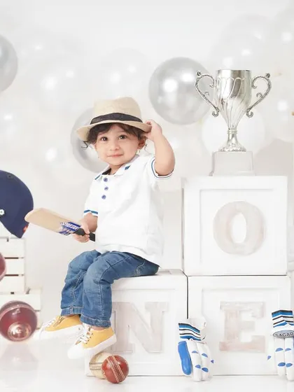 The little champion poses with his trophy in a full cricket-themed setup, complete with 'ONE' blocks for his first birthday.