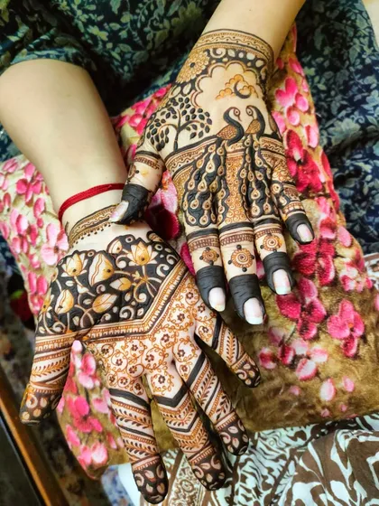 A creative design with one hand featuring peacocks under a tree and the other a floral vine pattern.