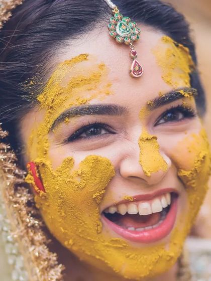 A close-up shot of the bride's ecstatic laugh, her face covered in haldi, capturing pure happiness.