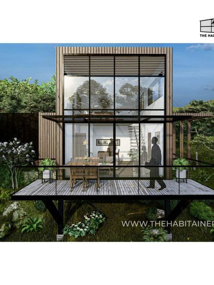 A render of a minimalist and functional container home design, nestled in a forest. The double-height glass facade and cantilevered deck create a stunning treehouse effect.