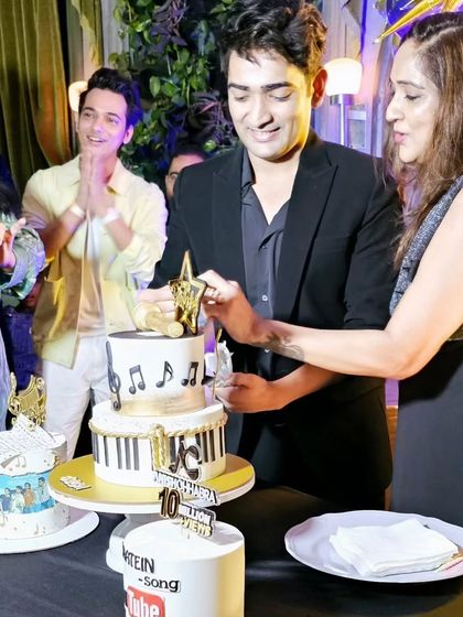 Anish Chhabra cutting his two-tier musical birthday cake, surrounded by friends and fellow artists.