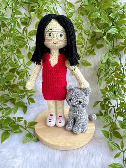 A thoughtful farewell gift for a niece heading off to higher studies. This replica doll in a red dress stands with her pet cat on a display base, a reminder of home she can take with her.