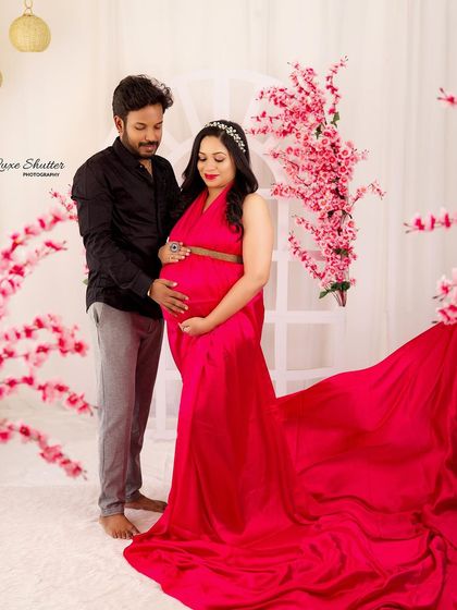A vibrant studio maternity portrait featuring a stunning pink gown with a long train. The floral backdrop complements the outfit, creating a look that is both bold and beautiful.