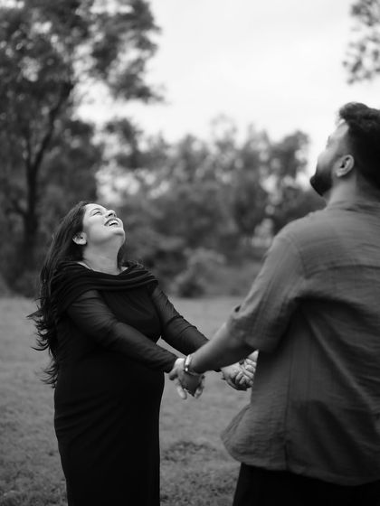 A black and white photo filled with pure joy. The couple holds hands and looks up, sharing a moment of genuine, uninhibited laughter.