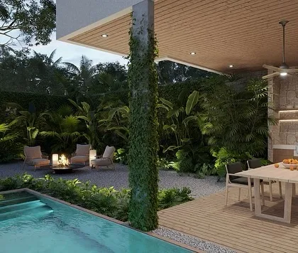 This patio design at night showcases a beautiful blend of features. We included a narrow lap pool, an outdoor kitchen and dining area, and a cozy fire pit lounge, all surrounded by dense, tropical-style greenery.
