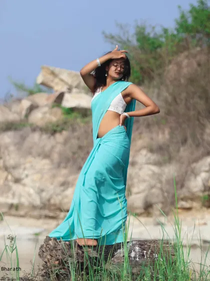 A powerful pose with the turquoise saree, shot against a rocky, natural background. The contrast between the soft fabric and the rough terrain is visually interesting.