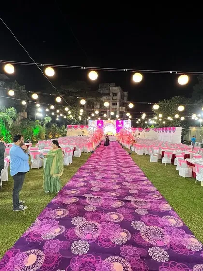 A long view of an outdoor reception aisle. The purple patterned carpet leads guests through the seating area directly to the main stage, creating a grand sense of arrival.