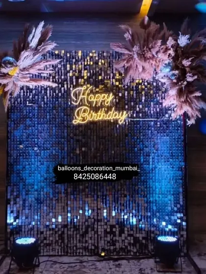 A stylish birthday photo booth with a blue sequin wall. The "Happy Birthday" neon sign is complemented by pampas grass arrangements for a modern, boho-chic look.
