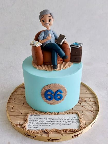 A personal and detailed cake for a 66th birthday. The topper is a custom figurine of the birthday person in his favourite chair, surrounded by his books.