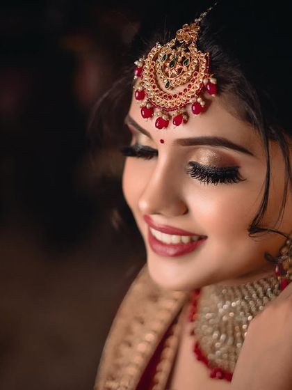 A close-up profile shot of the bride, highlighting her flawless makeup, intricate maang tikka, and elegant earrings. Her gentle smile completes this stunning portrait. (Duplicate of 101)