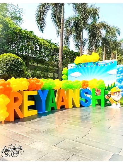 Large, colourful 3D letters spelling out the birthday boy's name, 'REYAANSH', with Paw Patrol characters integrated into the design. This makes for a great, personalized photo backdrop.