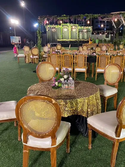 A view of the guest table arrangement. The combination of gold sequin tablecloths and classic wooden chairs on the green lawn created a look of understated luxury for this formal congratulatory dinner.