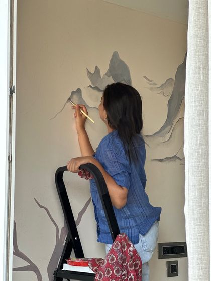 On a stepladder, reaching for the higher parts of a mountain mural. Every artwork, no matter the scale, is built from these small, simple, and sacred gestures.