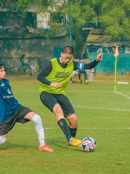 A player in a training bib skillfully maneuvers the ball away from a defender who is attempting a slide tackle.