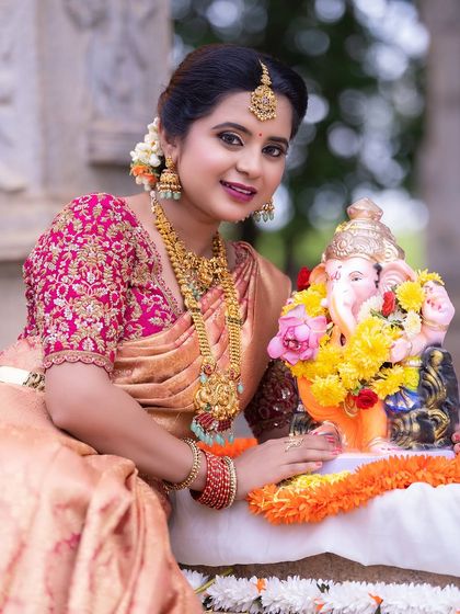 A model celebrating with a Ganesha idol, adorned in our layered temple jewellery. This set includes a choker, a longer necklace, and matching jhumkas.