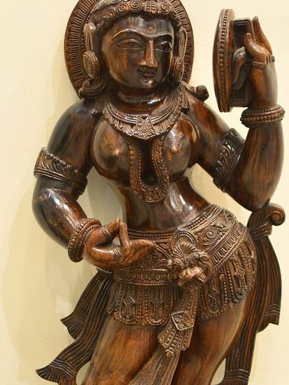A polished dark wood sculpture of an Apsara, showcasing the intricate details of her jewelry and flowing attire. Her serene expression draws you into her celestial world.