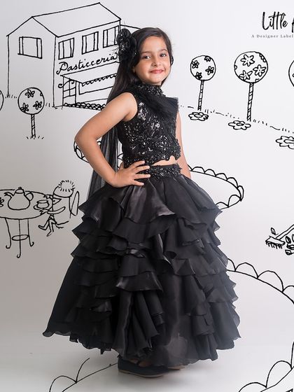 A little girl in a black ruffled lehenga against a fun, illustrated background, showing our playful side.