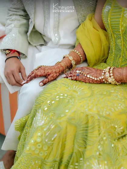 A close-up of the bride's hands, adorned with beautiful henna and jewelry, resting with the groom's. A quiet moment of connection during the Mehendi ceremony.