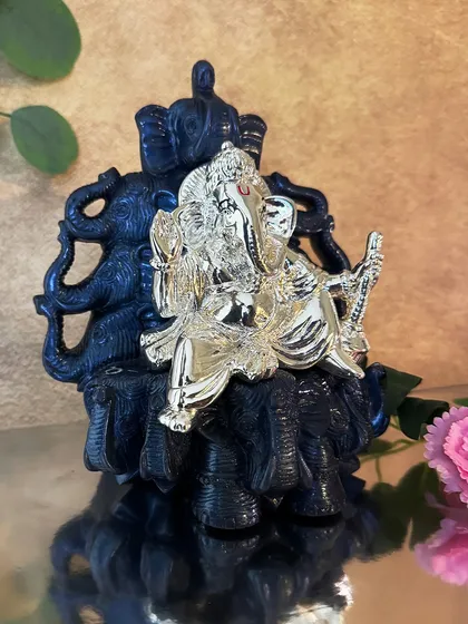This silver-plated Ganesha idol sits upon a dark, intricately carved elephant throne. The contrast between the radiant silver and the dark base makes this a visually striking piece of devotional art.