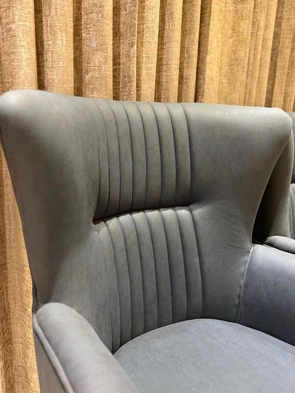 A pair of slate-blue high-back armchairs. The vertical channel tufting and winged design create a sense of modern elegance and provide comfortable, supportive seating.