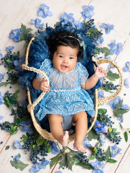 A beautiful overhead shot of a baby girl in a basket, surrounded by a sea of blue flowers. It's a creative and stunning way to capture a milestone.