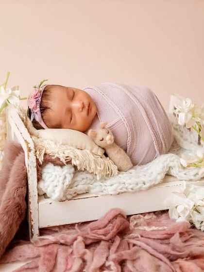 This baby is gently wrapped and posed in a miniature bed. The soft lavender and pink tones of the fabrics create a dreamy and feminine portrait.