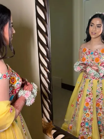 A bride looking in the mirror, her hair styled in soft waves with a floral crown. This is a perfect look for a bride who wants to feel like a princess on her Mehendi day.
