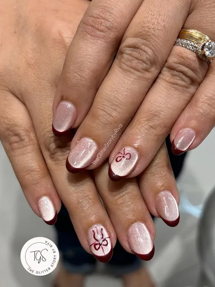 A festive French manicure with a twist. This set uses a shimmery cat-eye base with deep red tips and hand-painted bow accents for a holiday-ready look.