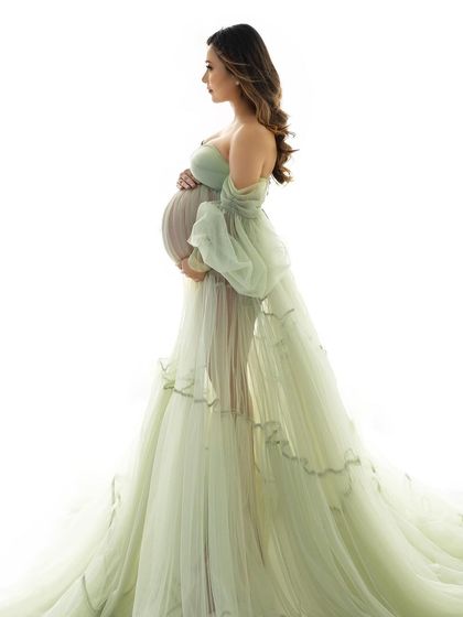 A high-key studio portrait that feels light and airy. The delicate fabric of the gown and the soft light beautifully highlight the baby bump.