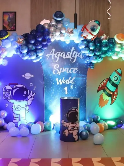 Take your child's party out of this world with a space and astronaut theme. This first birthday setup for Agastya includes a custom "Space World" backdrop, astronaut cutouts, and a balloon arch in shades of blue and silver to create a stellar celebration.