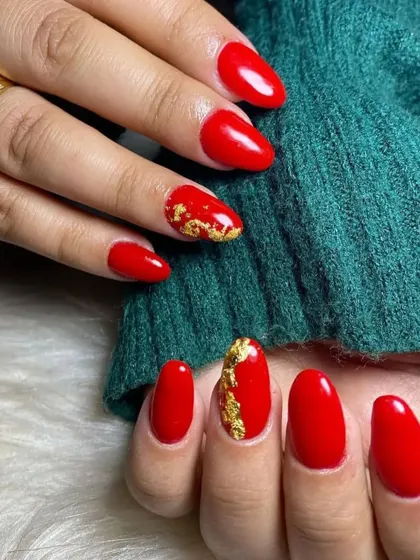 A vibrant red manicure on short, rounded nails, with a touch of gold foil on the accent finger for a festive look.