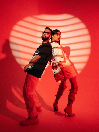 A full-length version of the back-to-back pose, showcasing the complete outfits. The composition is balanced and strong, highlighting the styling from head to toe.