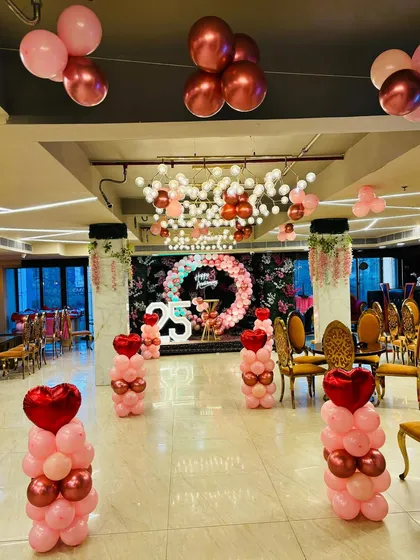 A grand 25th anniversary celebration in a banquet hall. The entrance is decorated with balloon pillars topped with heart balloons, leading to the main stage.
