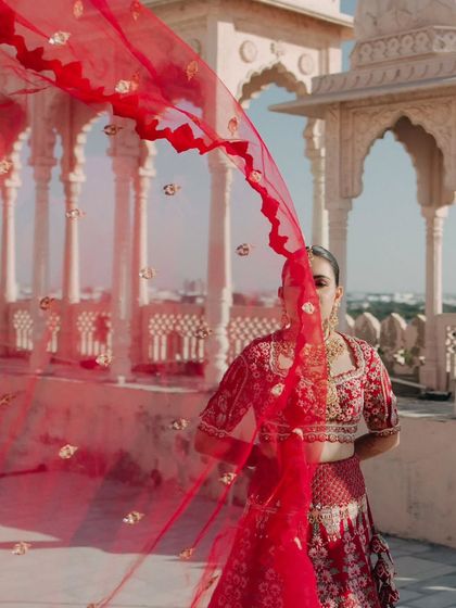 An artistic shot of the bride, her face partially hidden by her flowing red dupatta, creating a sense of mystery and grace.